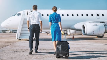 Man and woman in aviation uniform are walking to plane stairway with luggage before departure