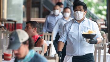 A waiter wearing a mask and gloves delivers food to a table to customers seated at an outdoor patio at a Mexican restaurant in Washington, DC, May 29, 2020. - Friday marks the beginning of phase one in the city with restaurants reopening following the sta