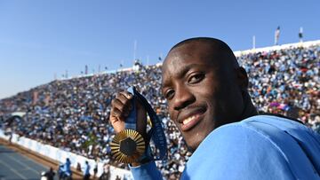 Olympic gold medallist, Botswana's Letsile Tebogo, who won the men's 200m athletics event during the Paris 2024 Olympic Games, holds his gold medal as he arrives on an open bus at the Botswana national Stadium during a welcoming ceremony in Gaborone on 13 August 2024. Botswana gave a rapturous welcome to Letsile Tebogo on Tuesday as the sprinter returned home with the southern African country's first ever Olympic gold medal. Families with children, elderly people and young supporters waved Botswana's sky blue, white and black national flag as the Olympic team landed back in the capital Gaborone. Hundreds of supporters had gathered at the small airport, benefiting from an impromptu half-day holiday declared by President Mokgweetsi Masisi to celebrate Tebogo's success. (Photo by Monirul Bhuiyan / AFP)