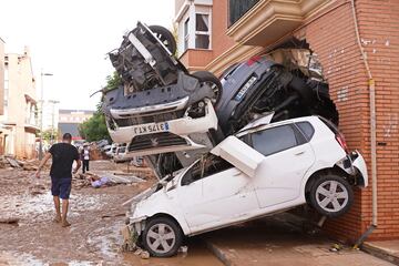 Un hombre camina junto a un grupo de coches amontonados tras las inundaciones en Massanassa, Valencia.