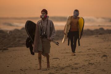 Un par de surfistas se protegen del humo del incendio Thomas declarado en el sur de California.