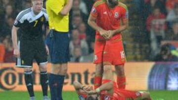 Gareth Bale, tendido sobre el césped, estira el gemelo con la ayuda de Joe Ledley.