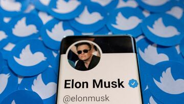Elon Musk's Twitter profile is seen on a smartphone placed on printed Twitter logos.