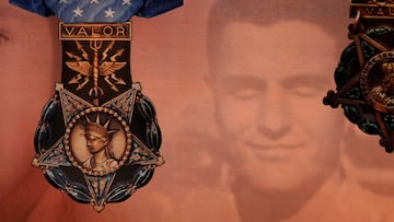 Una gran Medalla de Honor de la Fuerza Aérea cuelga junto a una gran Medalla de Honor del Ejército frente a un lienzo de pared a pared que muestra el rostro de Richard Etchberger y los símbolos del galardón.