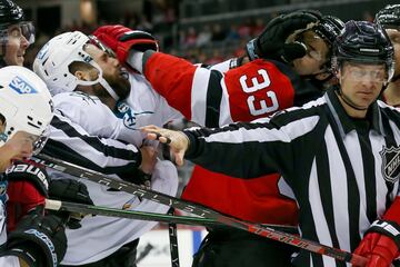 Espectacular imagen de la NHL, en la que el ala izquierda de los San Jose Sharks, Jonah Gadjovich (de blanco, con el 42) y el defensa de los New Jersey Devils Ryan Graves (de rojo, con el 33) se enganchan en una trifulca. Es un partido de hockey hielo, aunque por la fotografía bien podría confundirse con un combate de boxeo.