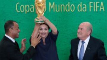 La presidenta de Brasil, Dilma Rousseff, sostiene el trofeo de la Copa del Mundo, junto al presidente de la FIFA, Joseph Blatter, y exjugador brasile&ntilde;o Caf&uacute;.