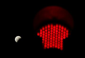 La luna parcialmente eclipsada se ve junto a un semaforo con la luz roja encendida en Columbia, Carolina del Sur, EE. UU.
