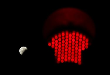 La luna parcialmente eclipsada se ve junto a un semaforo con la luz roja encendida en Columbia, Carolina del Sur, EE. UU.