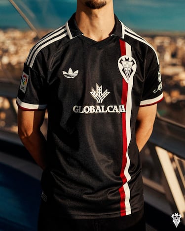 La camiseta está inspirada en la estética que marcó al Albacete Balompié de los años noventa y principios de los 2000, una etapa en la que el club consolidó su identidad en la élite y vivió momentos inolvidables como los ascensos de 1991 y 2003. Aquellos años quedaron ligados al liderazgo de Benito Floro al frente del ‘Queso Mecánico’ y a protagonistas como Zalazar, Conejo, Delfi Geli, Santi Denia o Jesús Perera, además de hitos como el histórico 3-1 ante el Atlético de Madrid o el 3-3 frente al FC Barcelona en Primera División. El diseño recupera el cuello polo característico de los noventa y el escudo retro ABP utilizado en aquella etapa, incorporando el color negro que el Albacete estrenó en 2001 como seña distintiva de los primeros años del nuevo milenio, reinterpretados con una mirada actual para reforzar el vínculo entre memoria, identidad albacetista y presente.