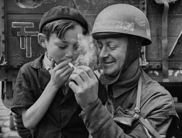 El cabo Fred Sicklong, un motociclista del XXX Cuerpo, 2.º Ejército británico enciende un cigarrillo para un joven francés en la ciudad liberada de Bayeux tras la Operación Overlord.