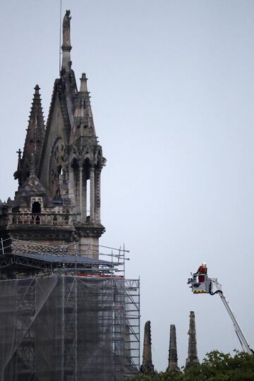 Un bombero trabaja subido en un elevador cerca de la parte de la estructura la catedral de Notre Dame