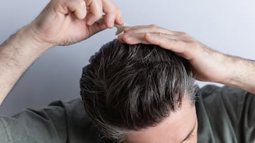 Close-up of unrecognizable man combing his toupee with his hands and a comb. Isolated on gray background. Hair styling and hair care concept