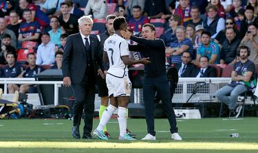 El entrenador del Barcelona, Xavi Hernández, habla con el jugador del Real Madrid, Vinicius, en la banda durante el partido ante la mirada de Carlo Ancelotti. 