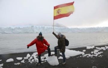 Alessi Pérez García (L) y José Díaz, ambos de España, posan con la bandera, en la costa del Lago Argentino, el glaciar Perito Moreno 