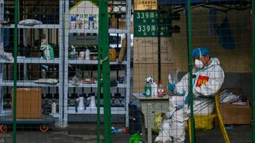 A worker wearing personal protective equipment (PPE) sits behind a fence in a residential area under a Covid-19 lockdown in the Xuhui district of Shanghai on June 16, 2022. (Photo by Hector RETAMAL / AFP) (Photo by HECTOR RETAMAL/AFP via Getty Images)