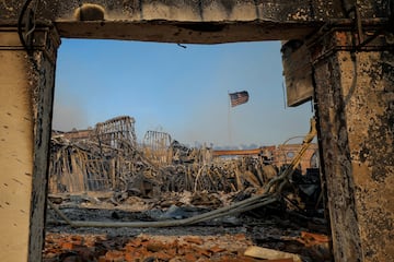 Una bandera estadounidense ondea entre los restos de edificios quemados mientras los fuertes vientos alimentan los devastadores incendios forestales en el rea de Los ?ngeles.