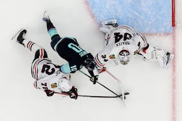 Matty Beniers #10 of the Seattle Kraken stickhandles against Alex Vlasic #72 and Petr Mrazek #34 of the Chicago Blackhawks