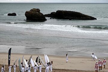 Los surfistas franceses Zoe Grospiron (centro) y Edouard Delpero (derecha) sostienen la llama olímpica durante el relevo de la antorcha en la playa entre Biarritz y Anglet.