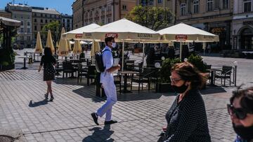 KRAKOW, POLAND - MAY 11: People walk past a restaurant garden at Krakow&#039;s UNESCO listed Main Square on May 11, 2021 in Krakow, Poland. From May 15, the obligation for people to cover their nose and mouth in outdoor public spaces will be lifted, bars 