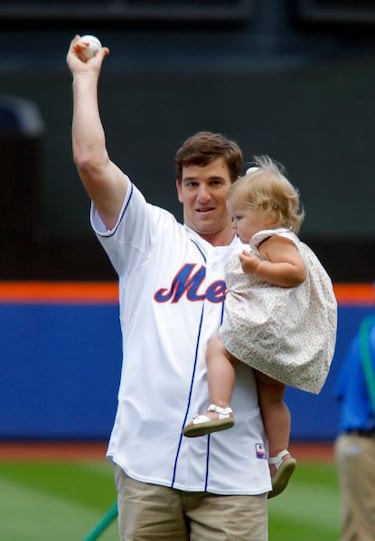 Mientras sosten赤a con su brazo izquierdo a su hija Ava, el quarterback de los Giants realiz車 su lanzamiento ante los Reds el 17 de junio de 2012.