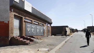 People walk past a closed liquor shop is seen in Soweto, on July 13, 2020. - South African President Cyril Ramaphosa on July 12, 2020 re-imposed a night curfew and suspended alcohol sales as COVID-19 coronavirus infections spiked and the health system ris