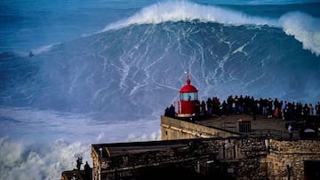 El surfista brasile&ntilde;o Vinicius Dos Santos (al fondo), surfeando una ola que podr&iacute;ai ser la m&aacute;s grande de la historia del surf, en Praia do Norte, Nazar&eacute; (Portugal) el 25 de febrero del 2022. En primer plano, mucha gente lo mira