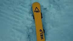 Tabla amarilla de snowboard de Help Snowboards rodeada de nieve.