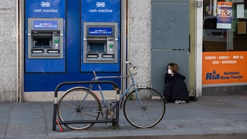 LONDON, ENGLAND - APRIL 15: A homeless woman wearing a face mask sits next to cash machines and an international money transfer shop in Dalston Kingsland on April 15, 2020 in London, United Kingdom. The Coronavirus (COVID-19) pandemic has spread to many
