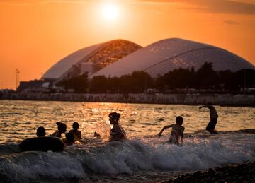 La gente se refresca en las olas del mar Negro mientras el sol se oculta detrás del estadio olímpico Fisht de Sochi.
