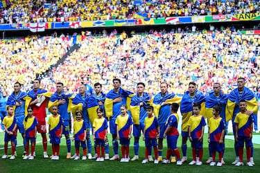 Los jugadores de Ucrania escuchan el himno de su país envueltos en su bandera.