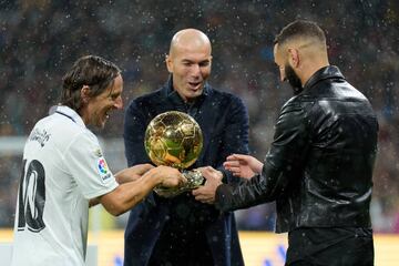 Modric y Zidane hacen entrega del Balón de Oro a Benzema, en un breve acto bajo la lluvia, el pasado sábado.