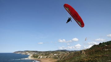 Yeray González durante un vuelo de parapente acrobático con un parapente rojo, sobre el mar y las montañas.