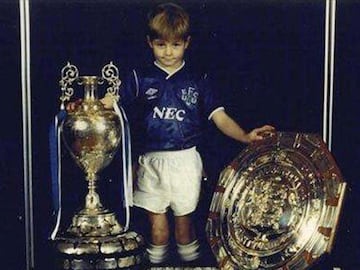 Steven Gerrard, leyenda del Liverpool, de pequeño posando con la camiseta y trofeos conseguidos por el Everton.