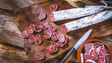 Spanish food backgrounds: overhead view of sliced and whole Spanish chorizo called "Fuet" on a cutting board shot on rustic wooden table. A kitchen knife complete the composition. High resolution 42Mp studio digital capture taken with SONY A7rII and Zeiss Batis 40mm F2.0 CF lens