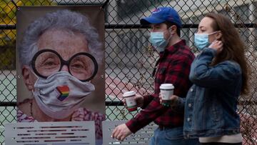 People walk past a picture by AJ Stetson, part of his &quot;Masked NYC&quot; exhibition, on the Upper West Side area of Manhattan New York on November 27, 2020. - Artists are taking over New York storefronts made empty by the coronavirus pandemic, receivi