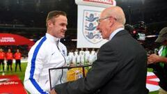 Charlton entrega la gorra conmemorativa a Rooney.