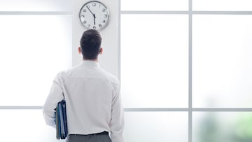 Businessman in the office staring at the clock, back view, time slave and stress concept