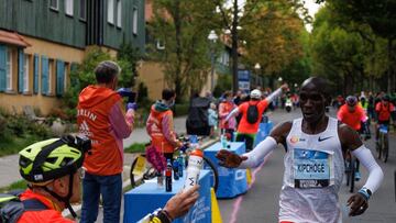 El atleta keniano Eliud Kipchoge recibe un bidón de manos de su aguado Claus-Henning Schulke durante el maratón de Berlín 2022.