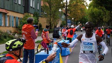 El atleta keniano Eliud Kipchoge recibe un bidón de manos de su aguado Claus-Henning Schulke durante el maratón de Berlín 2022.