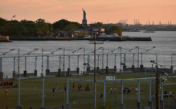  Un partido de fútbol durante la puesta de sol en el Brooklyn Bridge Park en Nueva York con la Estatua de la Libertad al fondo.