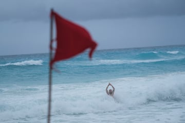 Un turista se baña en una playa mientras una bandera roja advierte a los bañistas de las condiciones peligrosas a medida que la tormenta tropical Helene se acerca a la península de Yucatán.