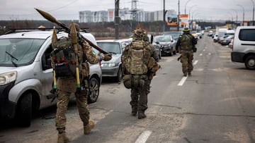 Ukrainian servicemen carry rocket-propelled grenades and sniper rifles as they walk towards the city of Irpin, north-west of Kyiv, on March 13, 2022.