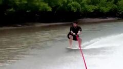 El surfista Italo Ferreira yendo a toda velocidad en aguas tranquilas y cogido de una cuerda con su tabla de surf. 