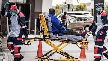 An emergency paramedic wearing full COVID-19 coronavirus personal protective equipment (PPE) flashes the victory sign as they arrive with a patient at the Greenacres Hospital in Port Elizabeth, on July 10, 2020. - Ambulances have to queue before patients