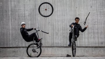 Un ciclista a una sola rueda levanta un dedo mientras su rueda delantera est&aacute; en el aire y a su lado, otro ciclista -tambi&eacute;n de wheelie- separa el manillar del resto del cuadro. 