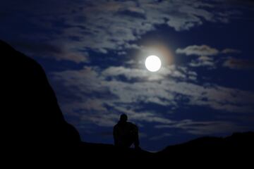 Un hombre se sienta en una roca mientras la luna llena sale en el desierto del Sahara a las afueras de Ouarzazate, Marruecos.