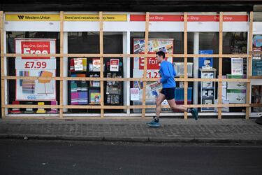 Un hombre pasa corriendo junto a una papelería que ha sido tapiada para proteger su fachada, antes del partido de fútbol.