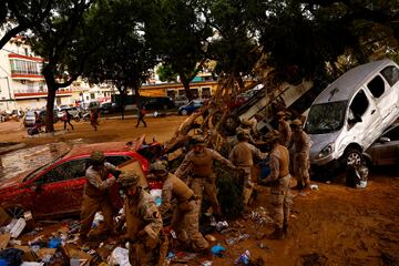 Miembros del ejército español trabajan para limpiar una calle cubierta de barro y escombros.