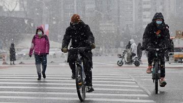 People ride their bicycles in the snow as they cross a street on a snowy day in Beijing on January 20, 2022. (Photo by Noel Celis / AFP)