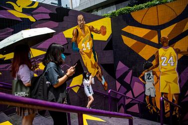 Unas mujeres con mascarilla toman fotos junto a un graffiti de Kobe Bryant y su hija Gigi en Guangzhou, al sur de China. La estrella de los Lakers falleció el pasado 26 de enero junto a su hija en un accidente de helicóptero y desde entonces los homenajes hacia ambos se han sucedido por todo el mundo; algunos, en forma de arte.